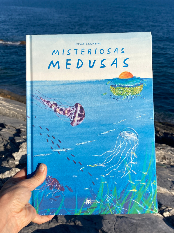 Libro Misteriosas medusas de Silvia Lazzarino, sostenido con una mano con el océano de fondo.