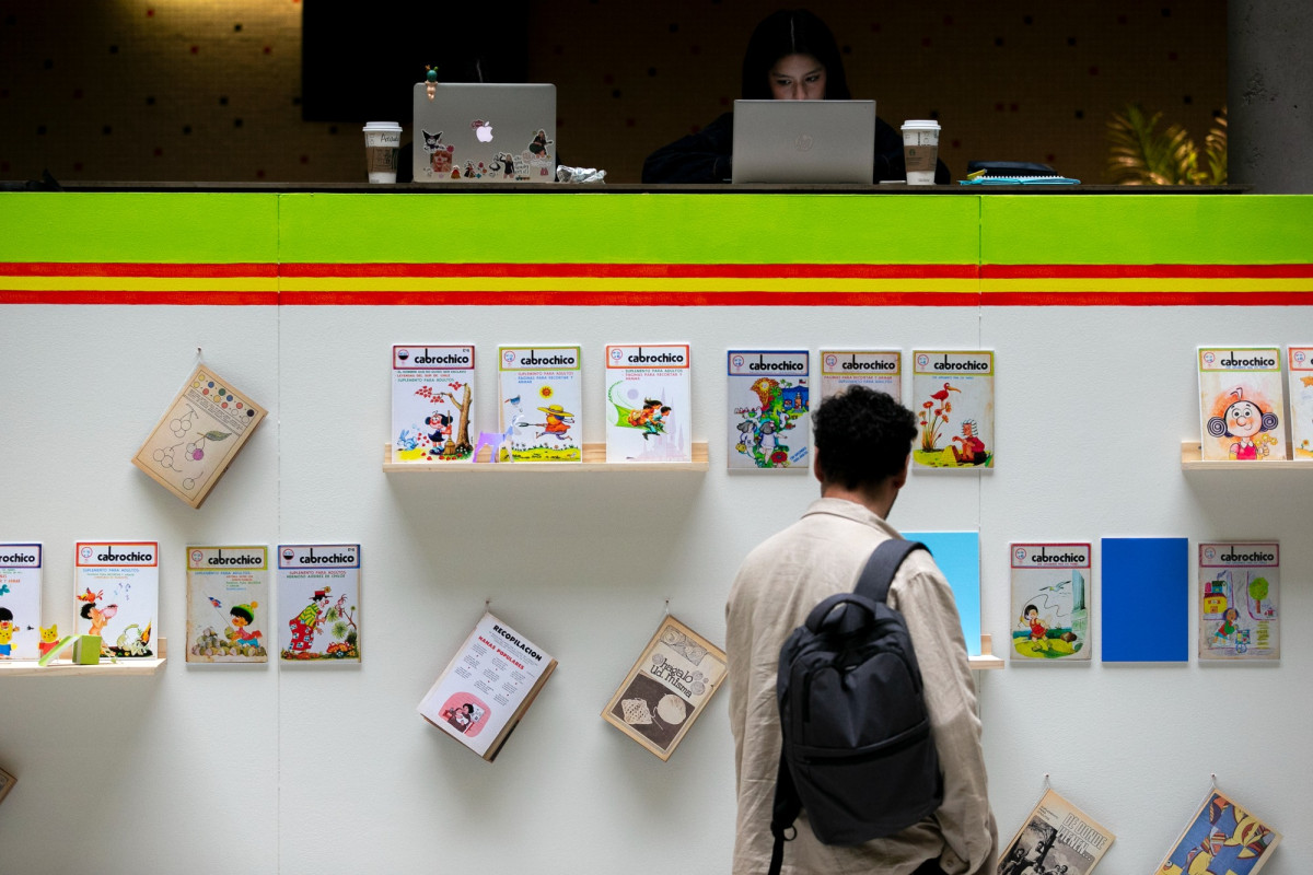 Hombre de espaldas, con una mochila, mirando un panel con portadas de la revista Cabrochico